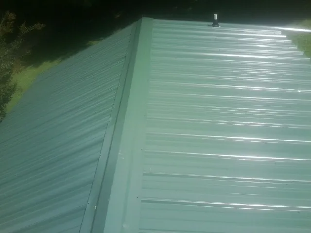 New green metal panels meeting at the ridge of a roof — Flat Roof Repair work by our crew in Woodland